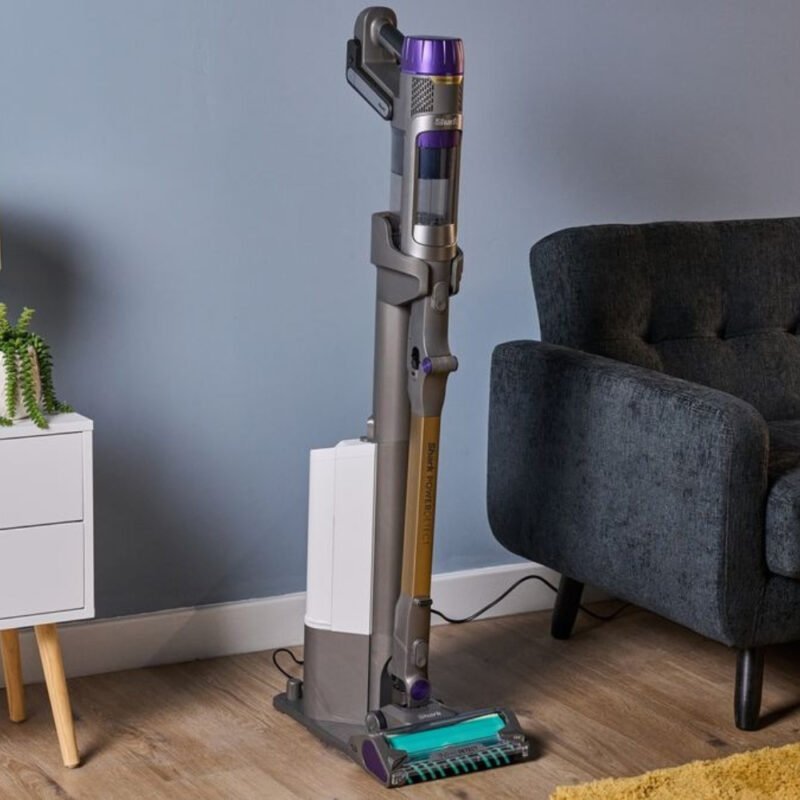 Shark cordless stick vacuum on its auto-empty dock in a living room with a hard floor and rug