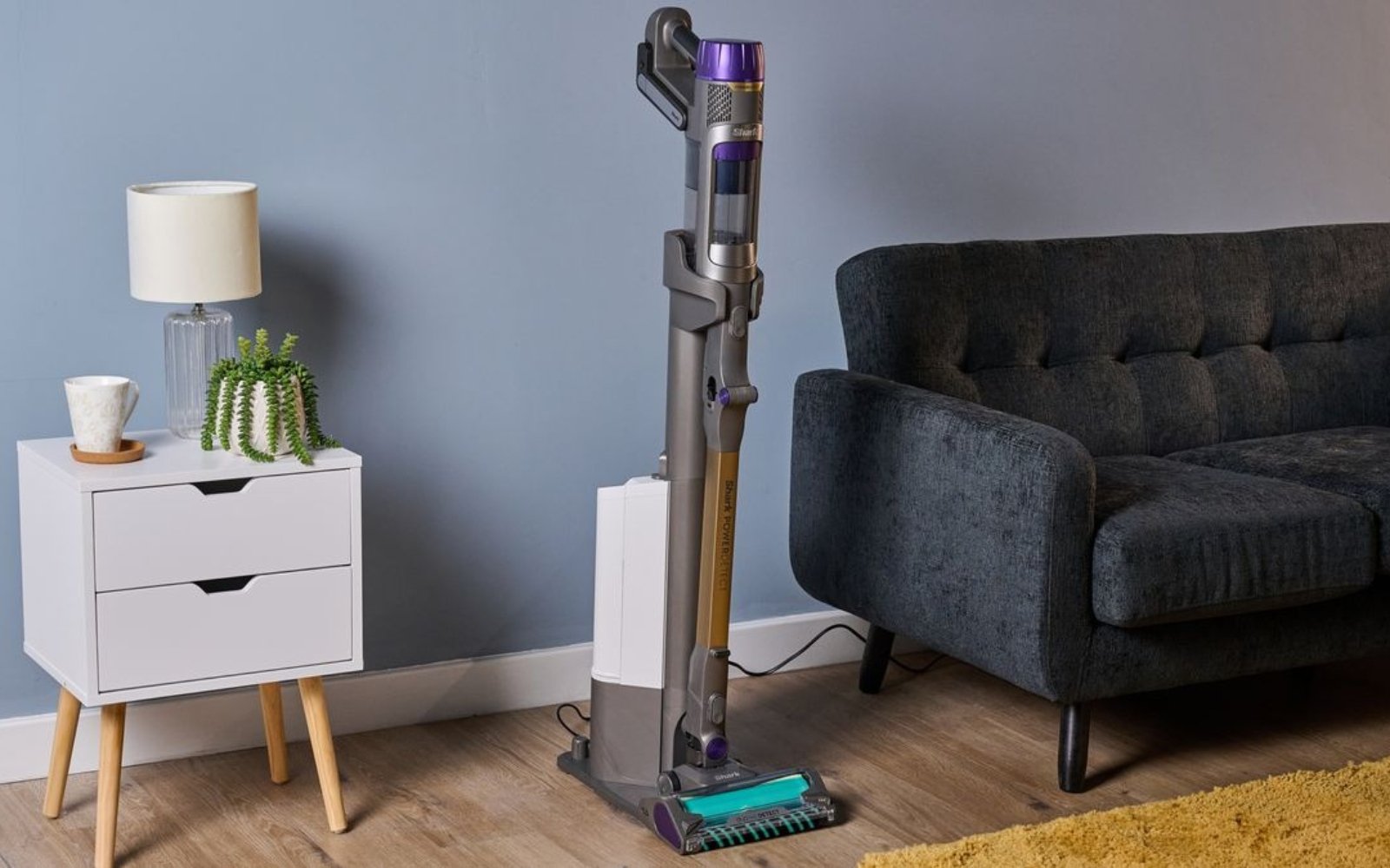 Shark cordless stick vacuum on its auto-empty dock in a living room with a hard floor and rug